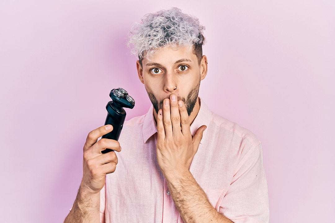 man with grey curly hair and beard using an electric shaver and making a grooming mistake that he should avoid.