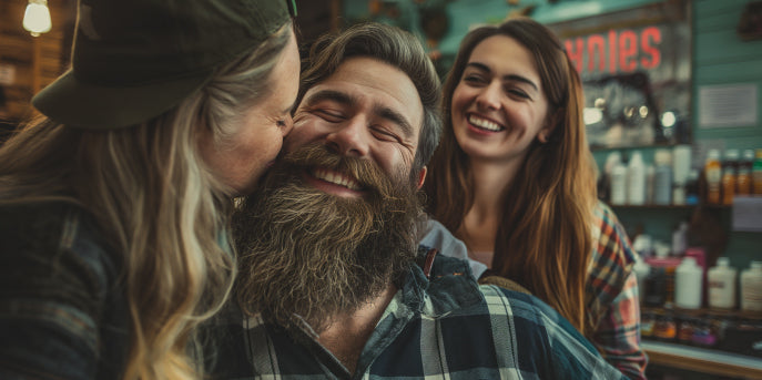 man with soft beard from beard oil having it smelled by his partner in barber shop